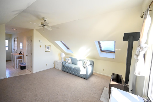 carpeted bedroom featuring a wood stove, lofted ceiling with skylight, and ceiling fan