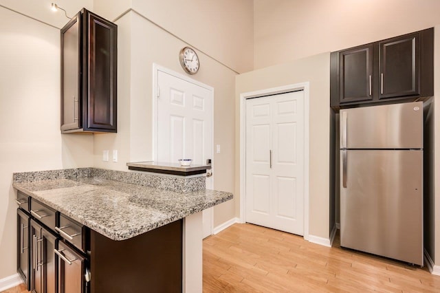 kitchen featuring stainless steel refrigerator, light stone counters, dark brown cabinetry, and light hardwood / wood-style floors