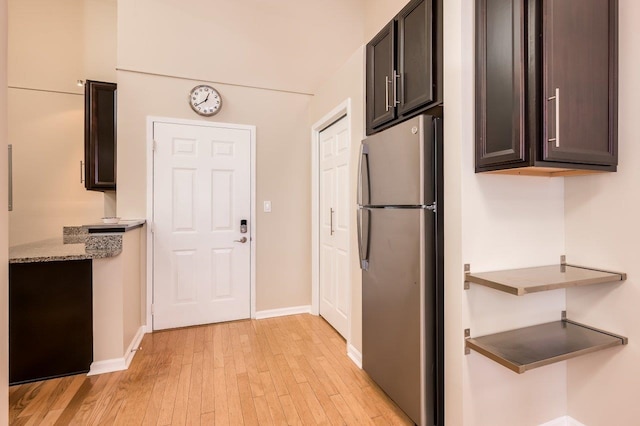 kitchen featuring light wood-type flooring, stainless steel fridge, dark brown cabinetry, and light stone counters