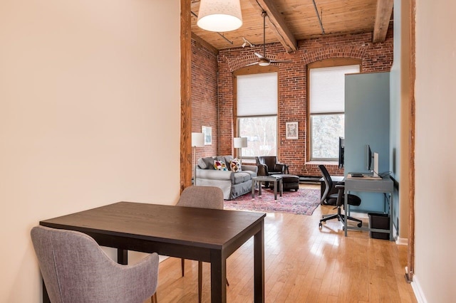 office area with wooden ceiling, light hardwood / wood-style flooring, a towering ceiling, beam ceiling, and brick wall