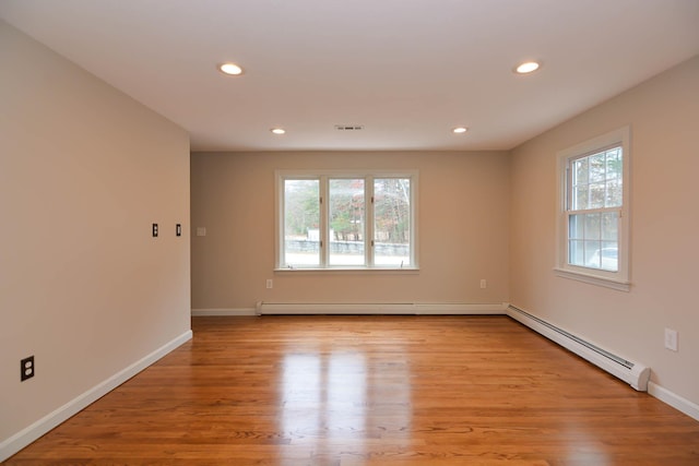 empty room with light hardwood / wood-style floors, baseboard heating, and a healthy amount of sunlight