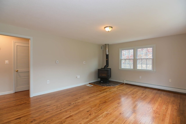 unfurnished living room featuring a wood stove, light hardwood / wood-style flooring, and a baseboard radiator