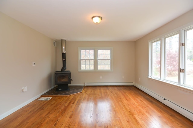 unfurnished living room with light wood-type flooring, a wood stove, and a baseboard heating unit