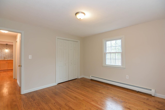 unfurnished bedroom with light wood-type flooring, a baseboard radiator, and a closet