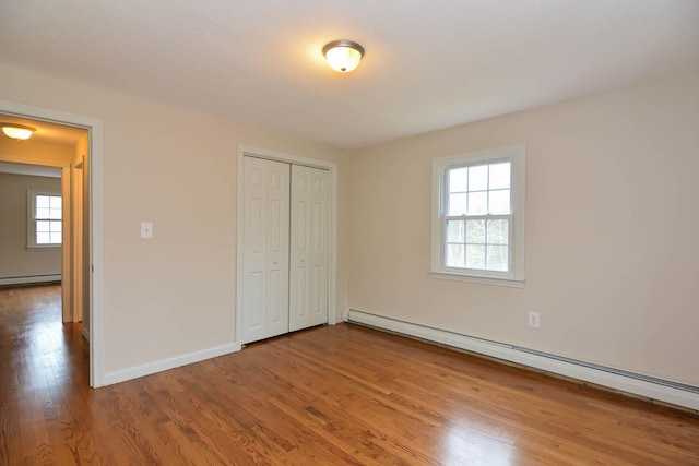 unfurnished bedroom with hardwood / wood-style flooring, a closet, multiple windows, and a baseboard heating unit