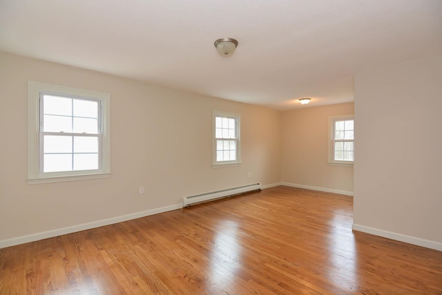 empty room featuring plenty of natural light, a baseboard radiator, and light wood-type flooring