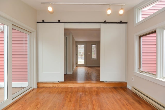 spare room with a wealth of natural light, a barn door, rail lighting, and baseboard heating