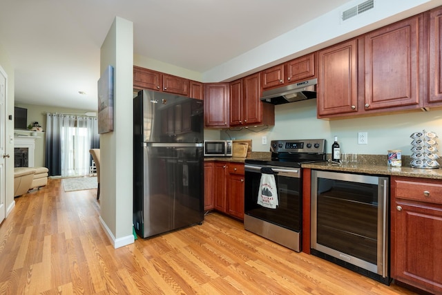 kitchen with dark stone countertops, beverage cooler, light wood-type flooring, and appliances with stainless steel finishes