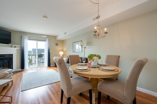 dining space with light wood-type flooring, a fireplace, and an inviting chandelier