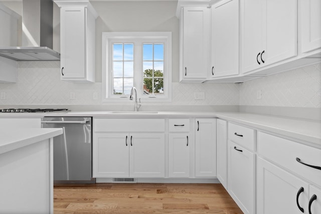 kitchen featuring stainless steel appliances, sink, wall chimney range hood, white cabinets, and light hardwood / wood-style floors