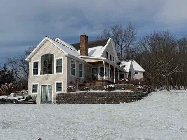 snow covered rear of property featuring covered porch