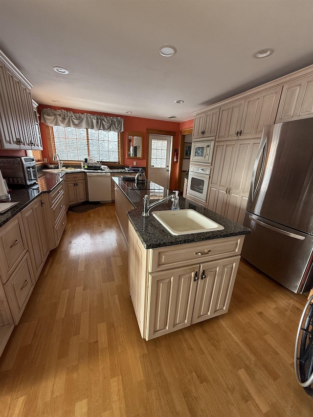 kitchen with sink, white appliances, an island with sink, and light wood-type flooring