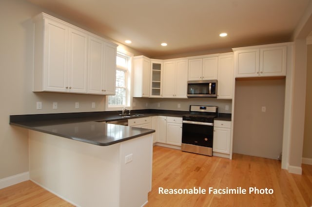 kitchen featuring sink, kitchen peninsula, appliances with stainless steel finishes, light hardwood / wood-style floors, and white cabinetry