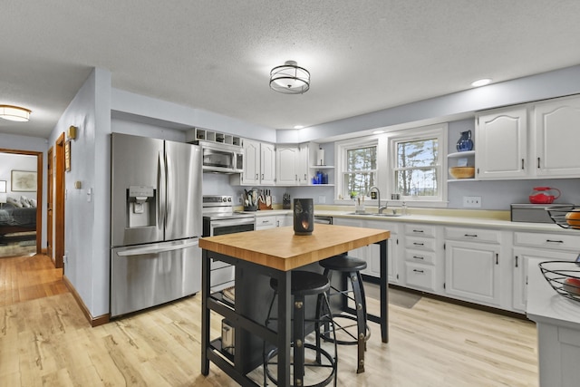 kitchen with white cabinets, sink, a textured ceiling, appliances with stainless steel finishes, and light hardwood / wood-style floors