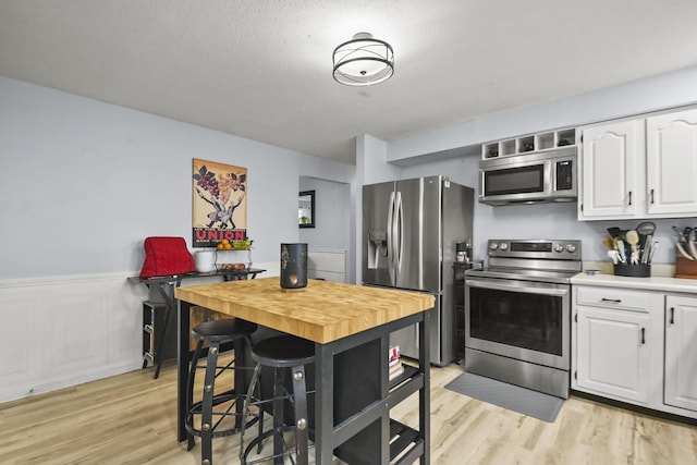 kitchen with a breakfast bar, a textured ceiling, stainless steel appliances, light hardwood / wood-style flooring, and white cabinetry