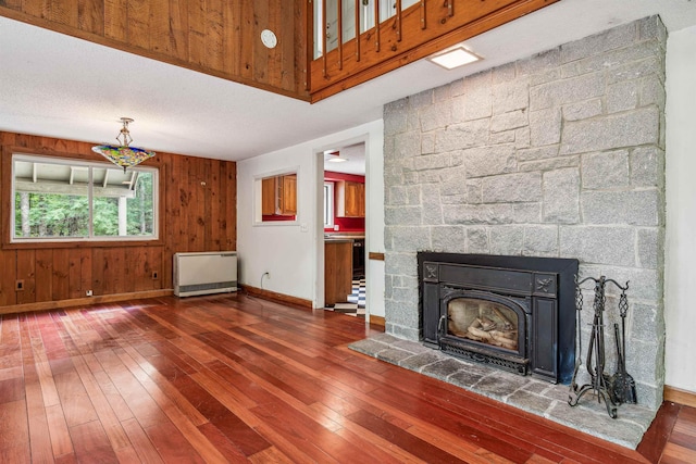 unfurnished living room featuring dark hardwood / wood-style flooring, radiator heating unit, a fireplace, and wooden walls