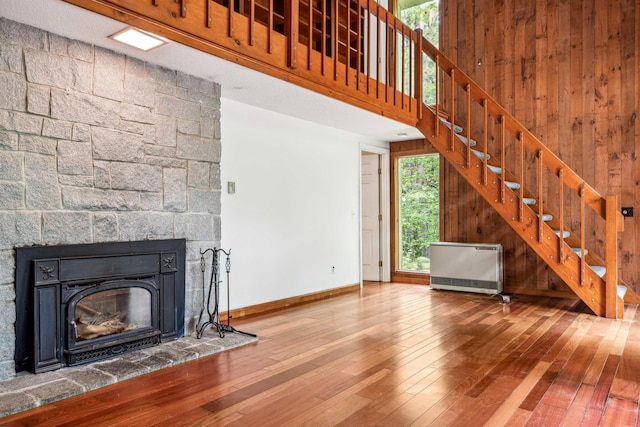 unfurnished living room with heating unit, wooden walls, a towering ceiling, and wood-type flooring