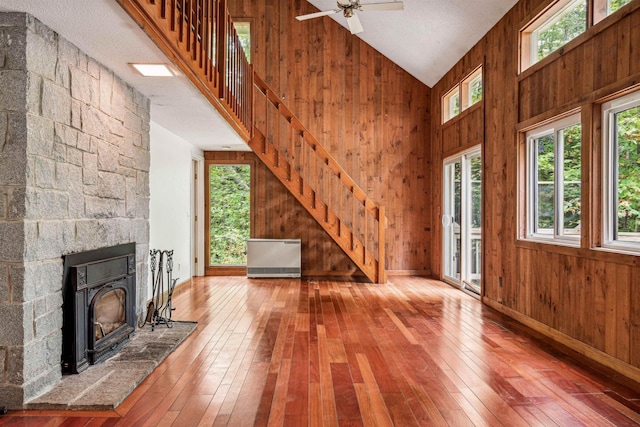 unfurnished living room with wooden walls, hardwood / wood-style floors, ceiling fan, and high vaulted ceiling