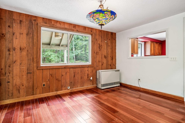 empty room with hardwood / wood-style flooring, a textured ceiling, wooden walls, and heating unit