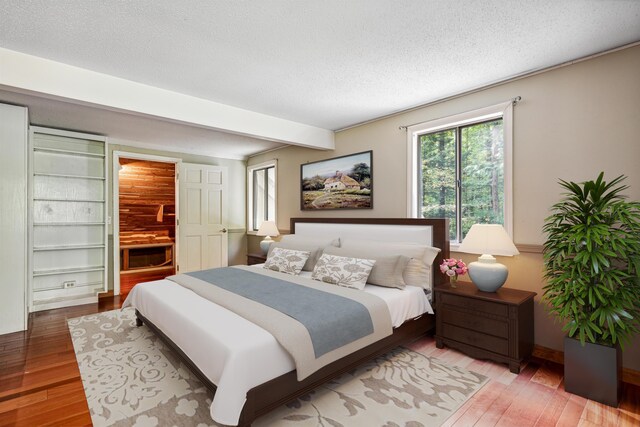 bedroom with hardwood / wood-style floors, a textured ceiling, and beam ceiling