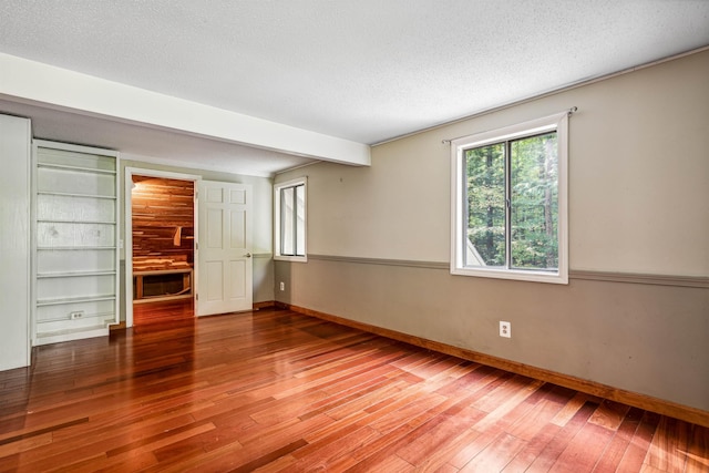 unfurnished room with beamed ceiling, built in shelves, a textured ceiling, and hardwood / wood-style floors