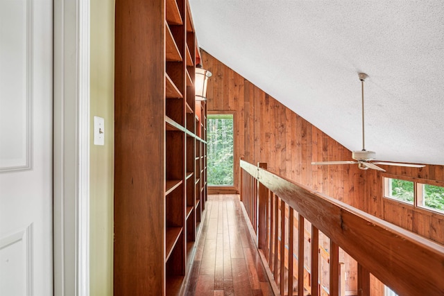 corridor featuring a textured ceiling, a wealth of natural light, lofted ceiling, and wood walls