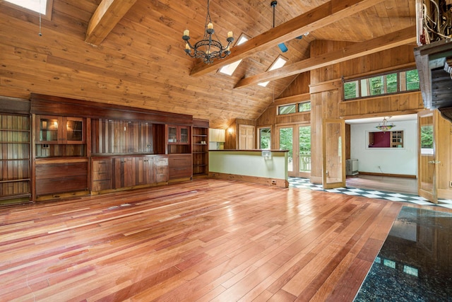 unfurnished living room with beam ceiling, a skylight, light hardwood / wood-style flooring, high vaulted ceiling, and wood walls