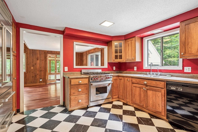 kitchen with sink, premium range, black dishwasher, wood walls, and a textured ceiling