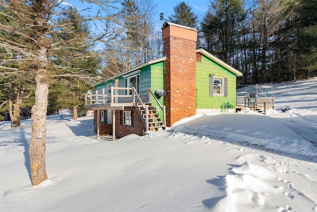 view of snow covered exterior with stairs, a deck, and a chimney