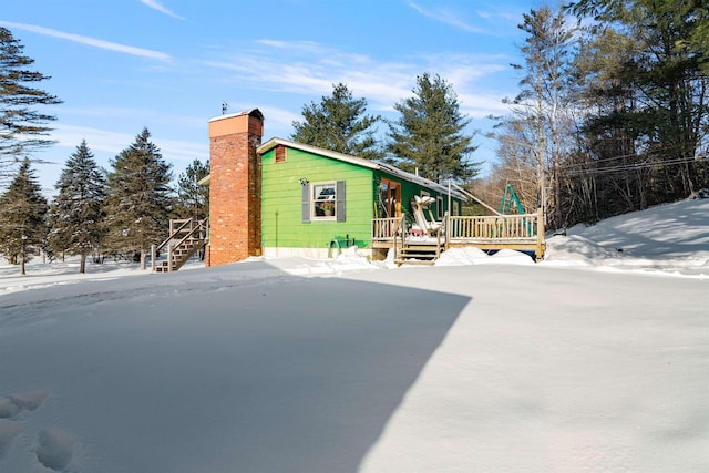 view of snow covered exterior featuring a wooden deck, a chimney, and stairway