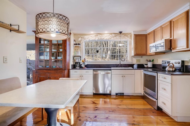 kitchen with appliances with stainless steel finishes, sink, white cabinets, light hardwood / wood-style floors, and hanging light fixtures