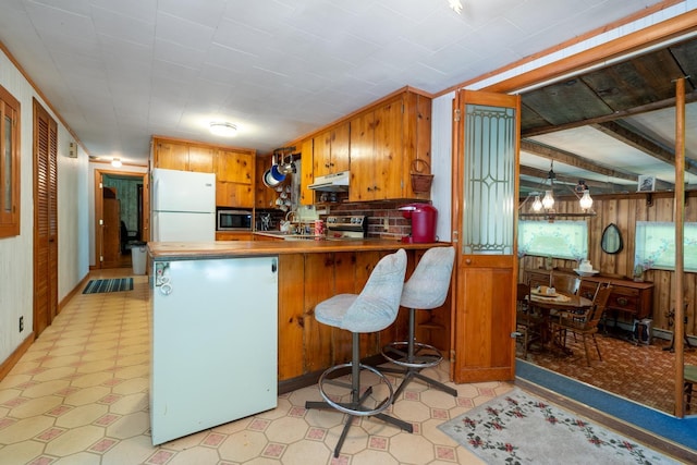 kitchen with kitchen peninsula, appliances with stainless steel finishes, a kitchen bar, and wooden walls