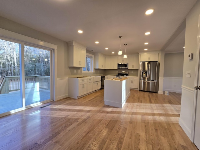 kitchen with a center island, hanging light fixtures, stainless steel appliances, light hardwood / wood-style flooring, and white cabinets