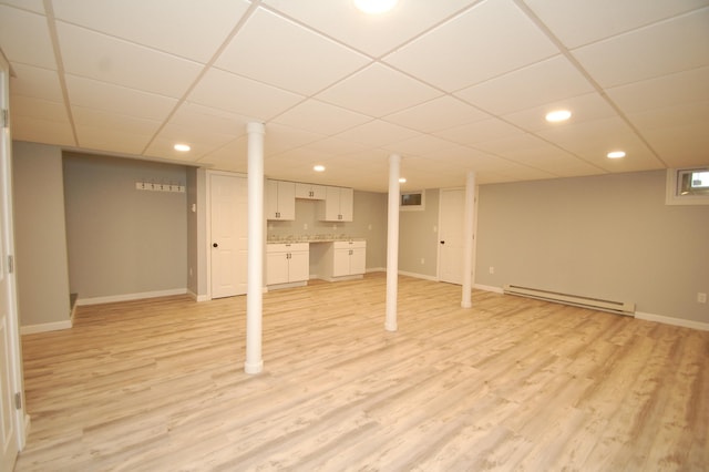 basement with a baseboard heating unit, a drop ceiling, and light wood-type flooring