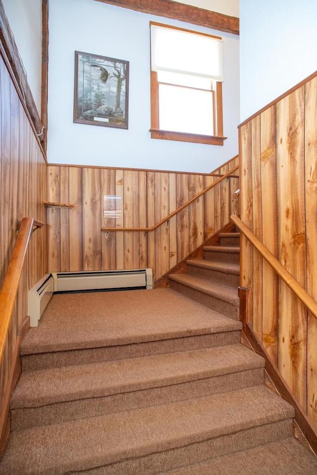 stairway featuring carpet flooring, wood walls, and baseboard heating