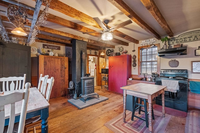 kitchen featuring beam ceiling, a wood stove, ceiling fan, black range with electric stovetop, and light hardwood / wood-style floors