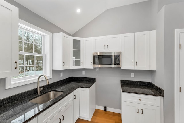 kitchen with white cabinetry, light hardwood / wood-style floors, dark stone countertops, vaulted ceiling, and sink