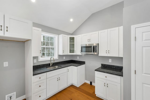 kitchen featuring lofted ceiling, sink, white cabinetry, light hardwood / wood-style flooring, and dark stone counters