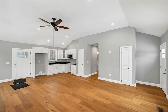 kitchen with ceiling fan, lofted ceiling, white cabinets, light hardwood / wood-style flooring, and sink