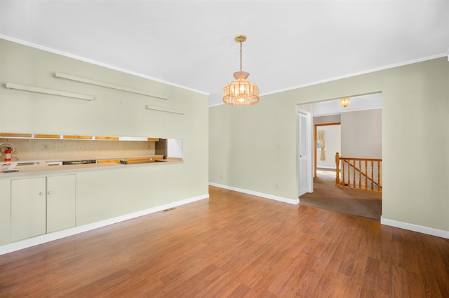 unfurnished living room featuring wood-type flooring, sink, crown molding, and a notable chandelier