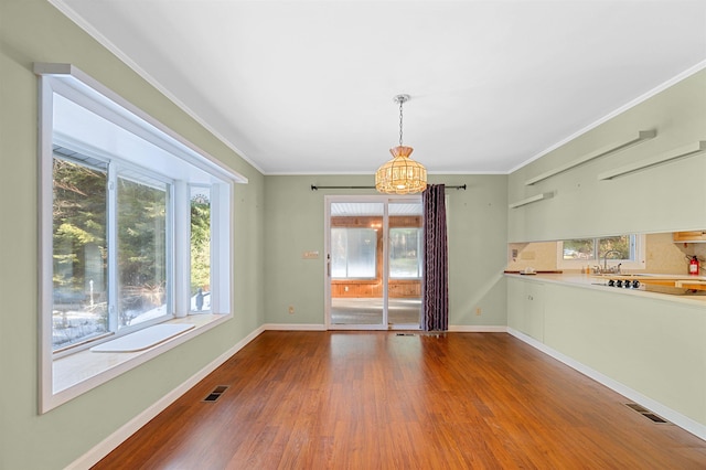 unfurnished dining area with wood-type flooring, ornamental molding, sink, and an inviting chandelier