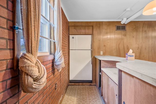 kitchen featuring wood walls, white fridge, ornamental molding, and brick wall