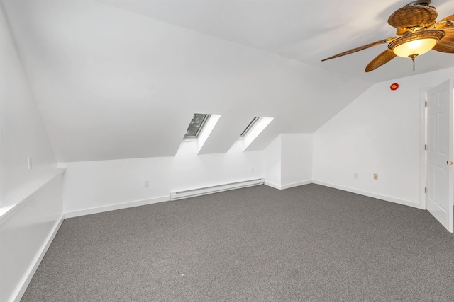 additional living space with dark colored carpet, ceiling fan, a baseboard heating unit, and vaulted ceiling with skylight