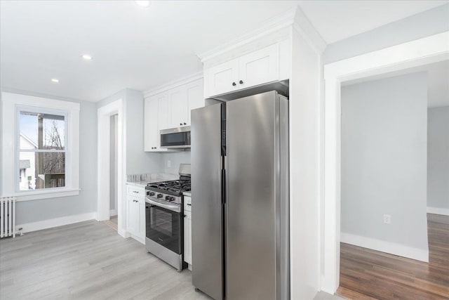 kitchen with radiator, white cabinets, stainless steel appliances, and light hardwood / wood-style floors