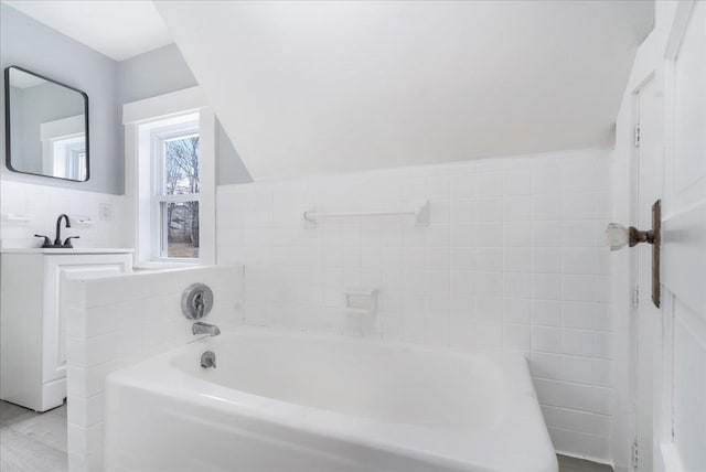 bathroom featuring a bathtub, lofted ceiling, and tile walls