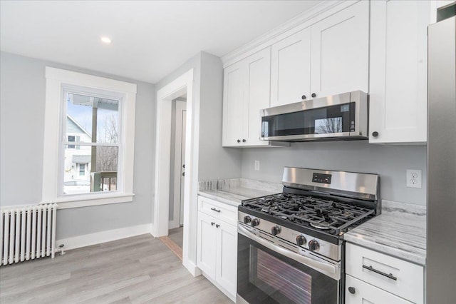 kitchen featuring stainless steel appliances, white cabinetry, radiator, and light stone counters