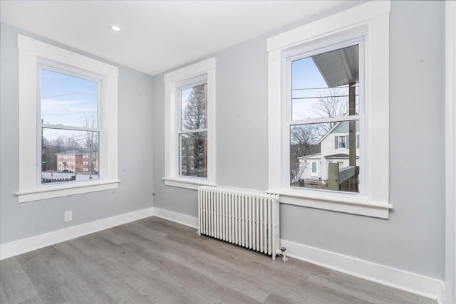 unfurnished room with radiator heating unit, a healthy amount of sunlight, and hardwood / wood-style flooring