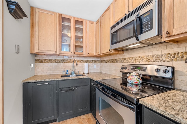 kitchen featuring decorative backsplash, light stone counters, sink, and appliances with stainless steel finishes