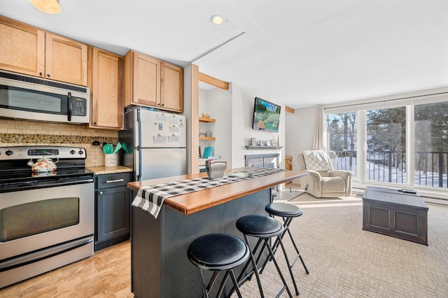 kitchen with backsplash, a kitchen breakfast bar, stainless steel appliances, and light hardwood / wood-style flooring