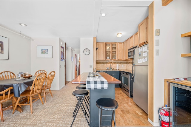 kitchen featuring beverage cooler, a kitchen breakfast bar, backsplash, light brown cabinetry, and appliances with stainless steel finishes